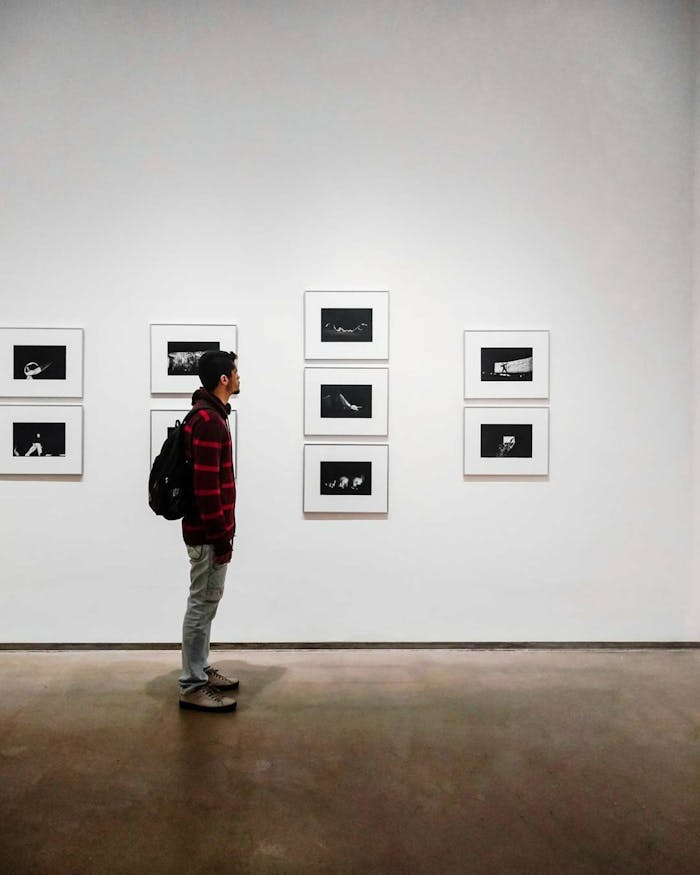 A man stands in an art gallery, observing framed black and white photographs.